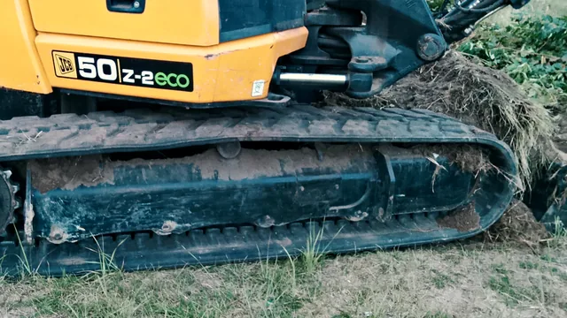 Zbliżenie na gumową gąsienicę i oznaczenie modelu koparki